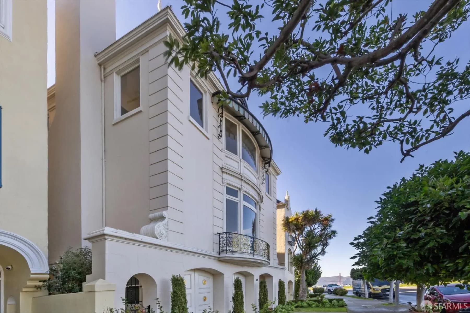 Cream stucco home with a curved bay window and iron balcony, Golden Gate Bridge in the distance