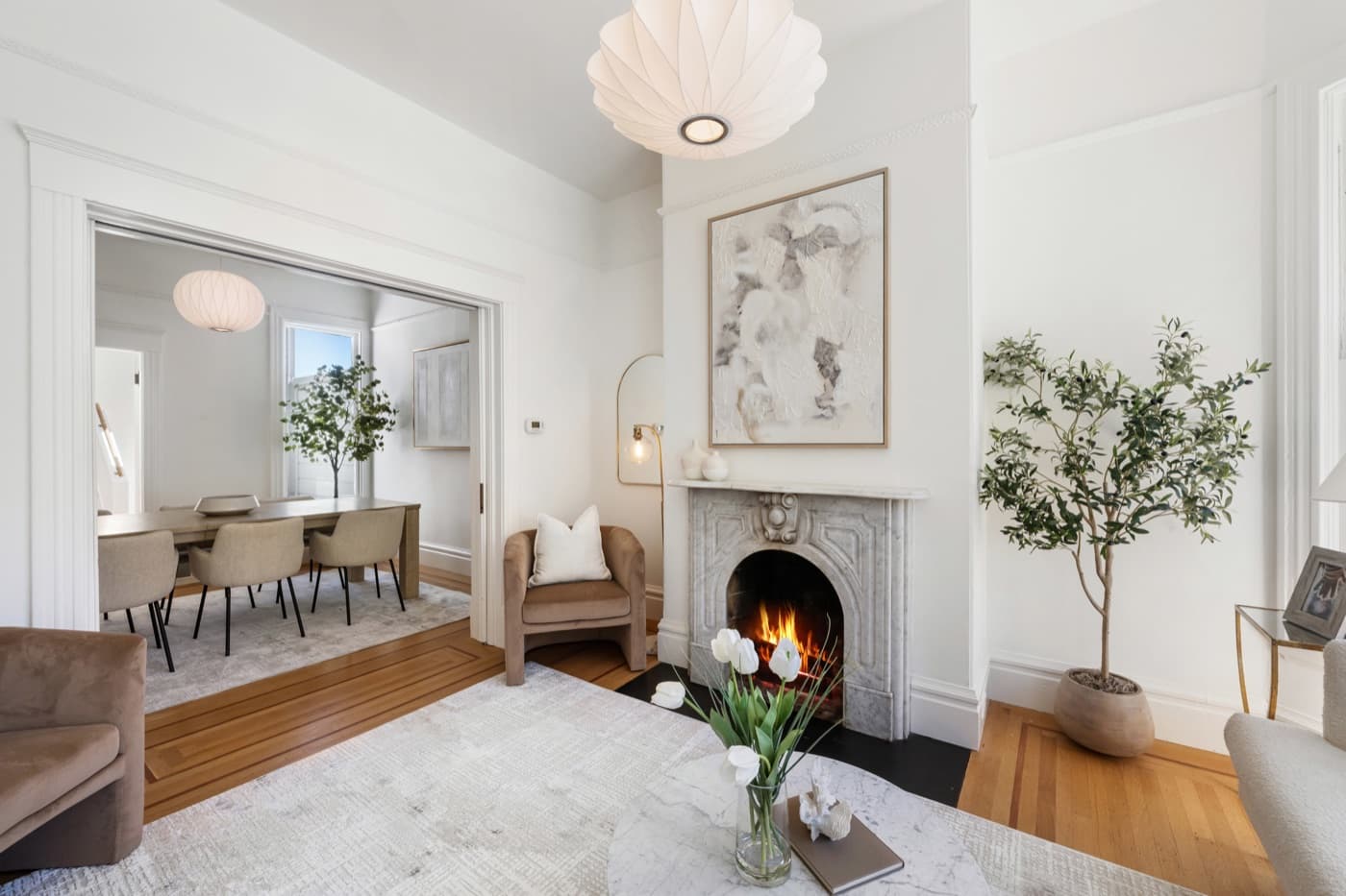 Staged parlor with a marble fireplace, olive tree and dining room beyond