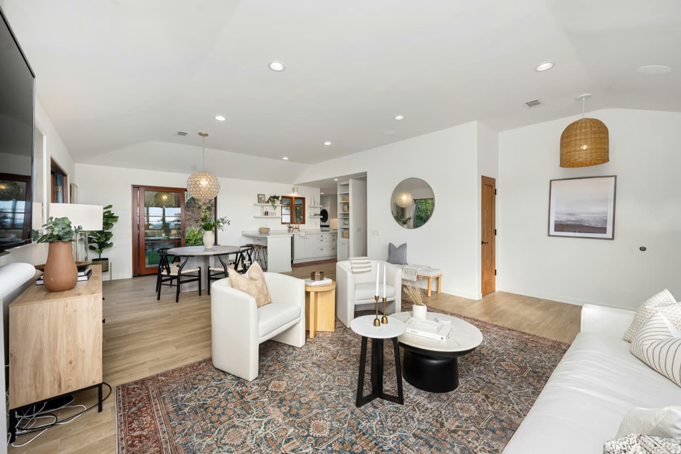 Staged open-plan living and dining room with a patterned rug, wicker pendant and view to the kitchen