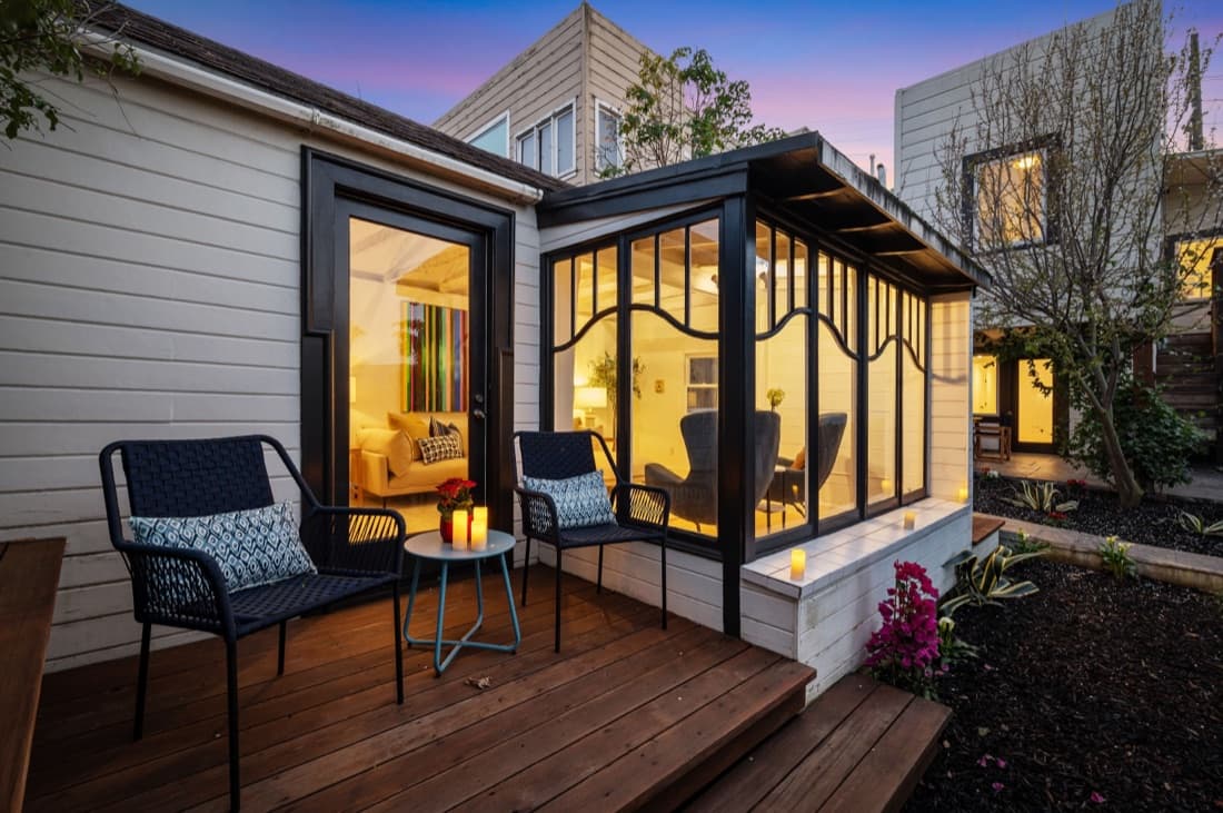 Rear deck at 567 Kansas Street at dusk with a glazed sunroom, seating and candlelight